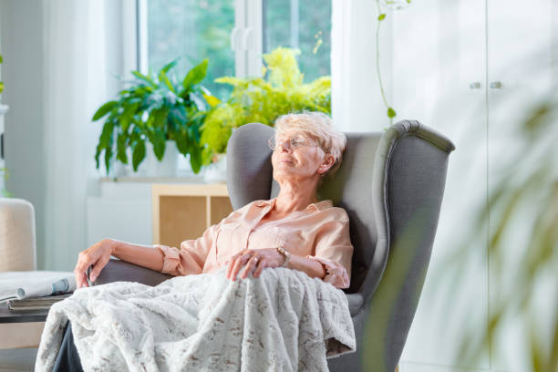 dame âgée se reposer dans un fauteuil dans sa chambre - vieux fauteuil photos et images de collection