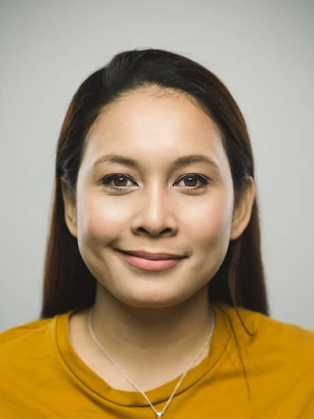 Real malaysian young woman with smirking expression Close up portrait of asian young woman with happy expression against white gray background. Vertical shot of malaysian real people smirking in studio with long brown hair. Photography from a DSLR camera. Sharp focus on eyes. smirking stock pictures, royalty-free photos & images
