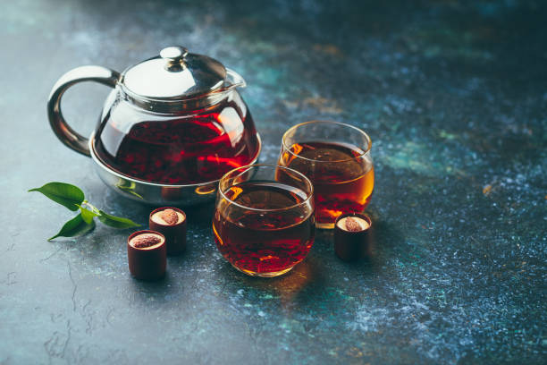 Glass cups of tea and teapot on the table Two glass cups and teapot with black tea and chocolate candies on dark background. black tea stock pictures, royalty-free photos & images