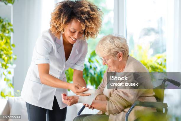 Home Nurse Bandaging The Wrist An Elderly Lady Stock Photo - Download Image Now - Nurse, Senior Adult, Bandage