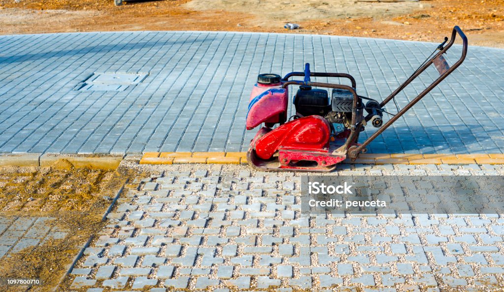 Vibrator with rubber plate for compacting paving with interlocking blocks Building - Activity Stock Photo