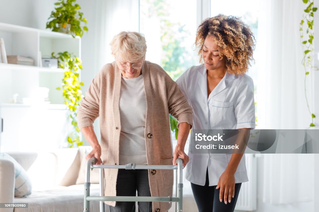 Nurse helping an elderly lady in using mobility walker Afro american female home nurse supporting senior woman in using mobility walker at home. Senior Adult Stock Photo