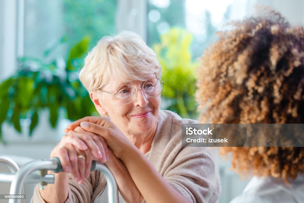Senior woman talking with female home caregiver Nurse supporting smiling and cheerful senior woman at her home, touching her hands. Adult Stock Photo