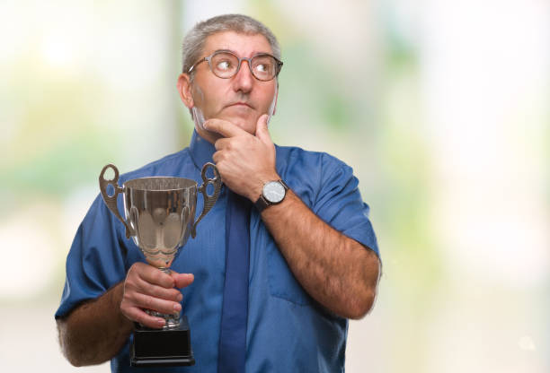 istock Handsome senior successful man holding trophy over isolated background serious face thinking about question, very confused idea 1097802228