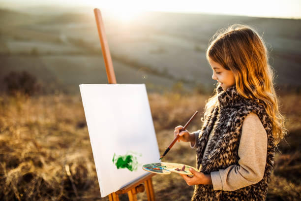 Happy little girl enjoying while painting in autumn day outdoors.