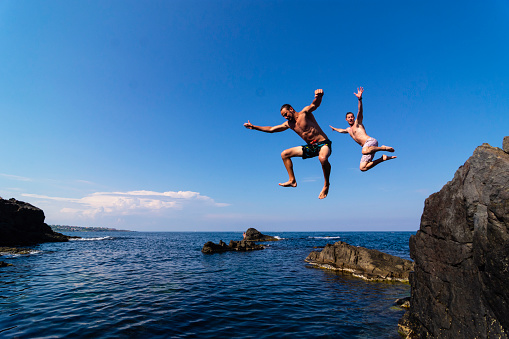 Two brave divers jumping off cliff into sea