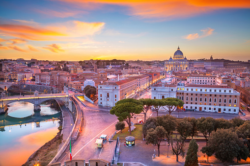 Beautiful bridge over river Tiber and distant view of the dome of the famous St. Peter's basilica during sunset in Rome, Italy