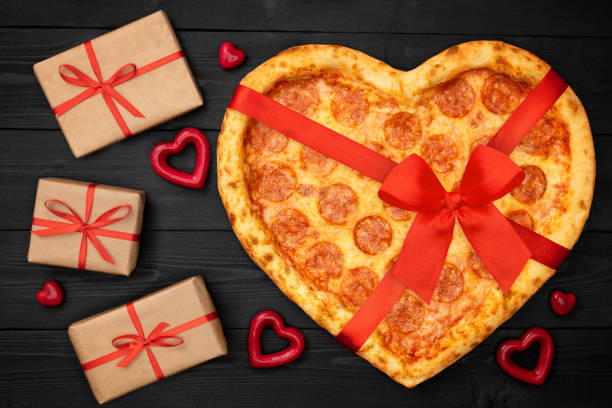 istock Pizza shaped heart with red bow ribbon and present box for Valentine's Day romantic concept on rustic dark black background. Top View. Flat lay 1097817538