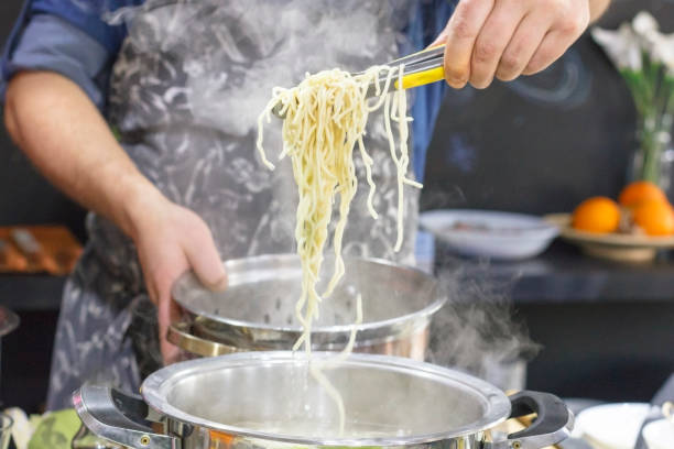 istock Chef takes out with slotted spoon hot steaming egg noodles from the pan 1097820366