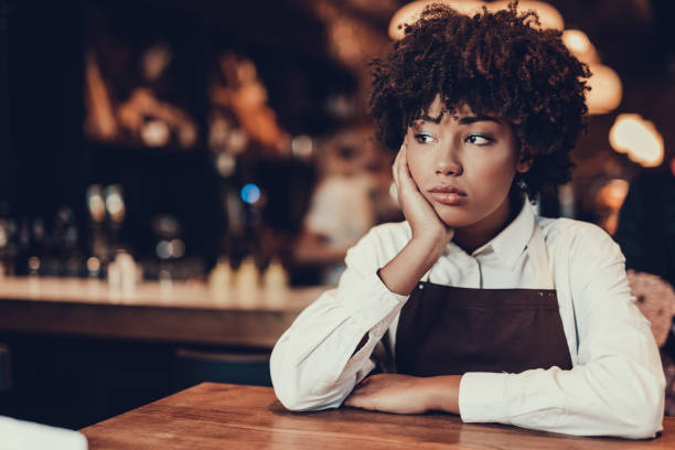 Tired young lady looking aside and sitting over table Portrait of upset waitress. She looking aside and sitting behind table while touching cheek by palm hand bad coffee stock pictures, royalty-free photos & images