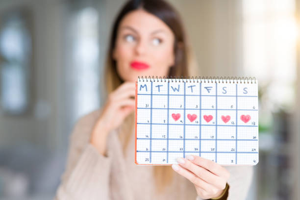 joven mujer hermosa celebración calendario de menstruación en casa cara seria pensar pregunta, idea muy confundida - photography ideas healthcare and medicine indoors fotografías e imágenes de stock