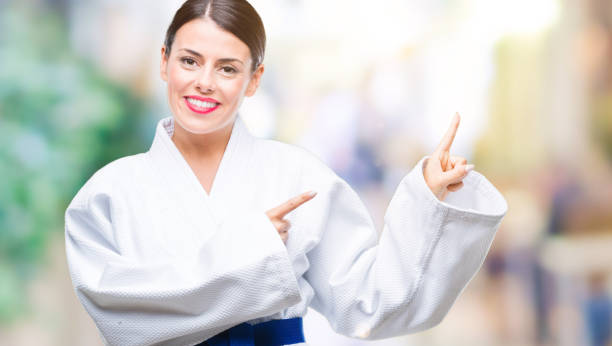 istock Young beautiful woman wearing karate kimono uniform over isolated background smiling and looking at the camera pointing with two hands and fingers to the side. 1097830708
