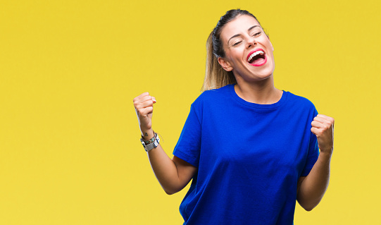 Young beautiful woman wearing casual blue t-shirt over isolated background very happy and excited doing winner gesture with arms raised, smiling and screaming for success. Celebration concept.