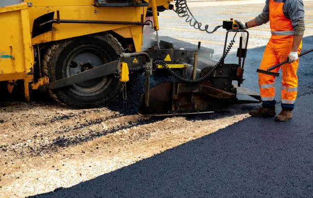 Workers regulate tracked paver laying asphalt heated to temperatures above 160 ° pavement on a runway