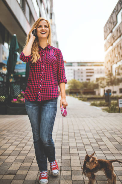 istock Woman using phone while walking with dog in the city 1097846284