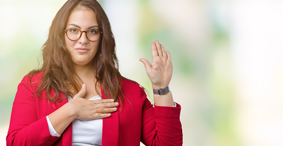 Beautiful plus size young business woman wearing elegant jacket and glasses over isolated background Swearing with hand on chest and open palm, making a loyalty promise oath