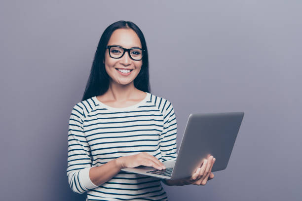 Portrait of nice cute attractive lovely straight-haired lady wearing striped pullover holding in hands laptop e-commerce video lessons isolated on gray pastel background Portrait of nice cute attractive lovely straight-haired lady wearing striped pullover holding in hands laptop e-commerce video lessons isolated on gray pastel background netbook stock pictures, royalty-free photos & images