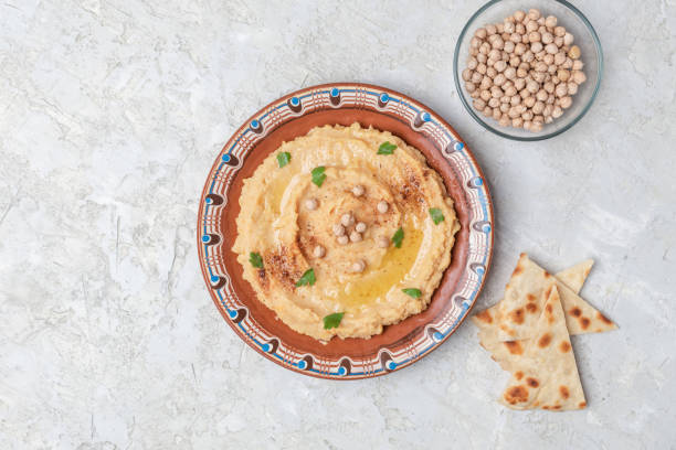 istock Hummus in a brown clay plate with a blue pattern. On the white table are vegetables, greens, triangular pieces of pita. Top view. Flat lay. 1097851574