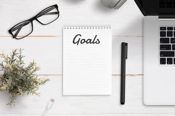 istock Writing annual goals on empty notepad. Office desk with laptop computer, and office supplies. Top view. 1097878500