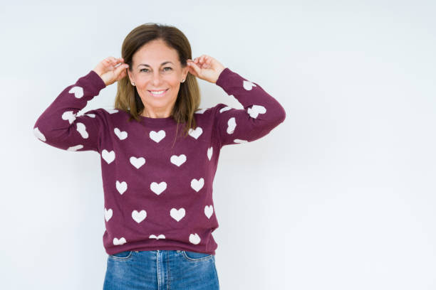 istock Beautiful middle age woman wearing heart sweater over isolated background Smiling pulling ears with fingers, funny gesture. Audition problem 1097878742