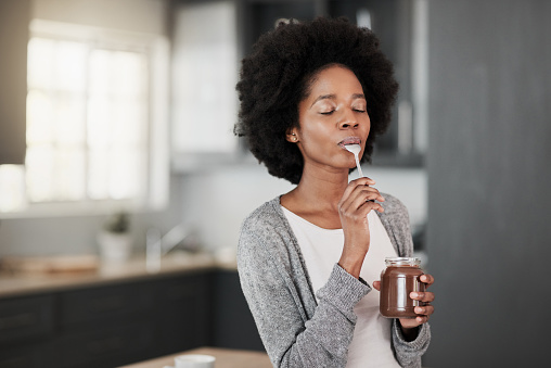 Shot of a young woman eating chocolate from a jar at home