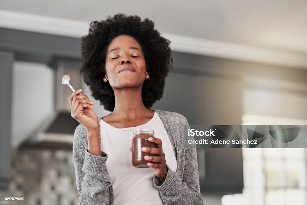 Starting the day the sweet way Shot of a young woman eating chocolate from a jar at home Tasting Stock Photo