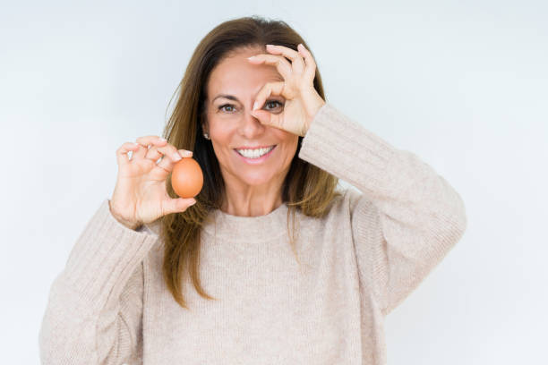istock Middle age woman holding fresh egg over isolated background with happy face smiling doing ok sign with hand on eye looking through fingers 1097880976
