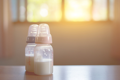 Baby bottle with milk and a measuring scale on the background of a lot of full bottles of breast milks, the most healthy food for newborn,vintage color