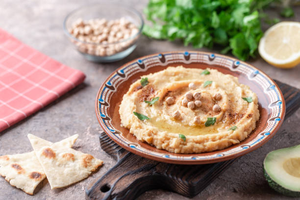 istock Hummus in a brown clay plate with a blue pattern. On the white table are vegetables, greens, triangular pieces of pita. Top view. Flat lay. 1097887338