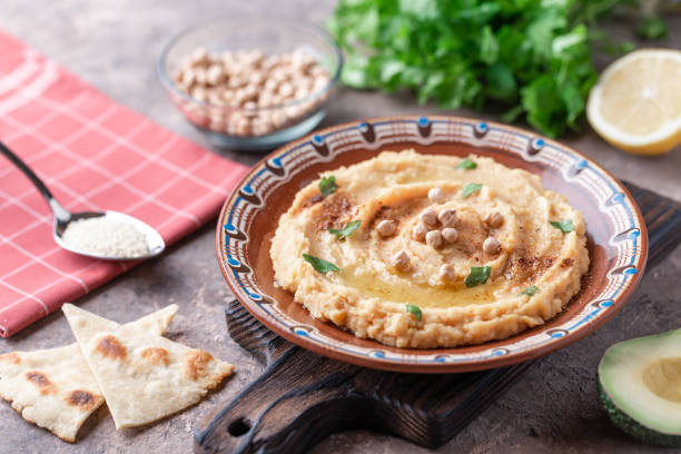 istock Hummus in a brown clay plate with a blue pattern. On the white table are vegetables, greens, triangular pieces of pita. Top view. Flat lay. 1097889144