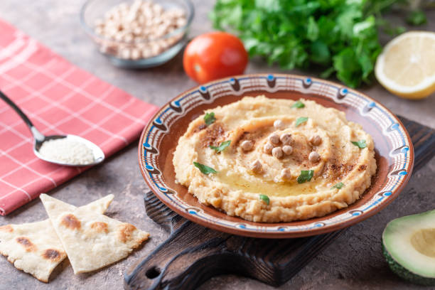 istock Hummus in a brown clay plate with a blue pattern. On the white table are vegetables, greens, triangular pieces of pita. Top view. Flat lay. 1097889856