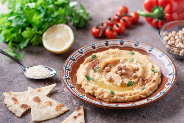 istock Hummus in a brown clay plate with a blue pattern. On the white table are vegetables, greens, triangular pieces of pita. Top view. Flat lay. 1097893220