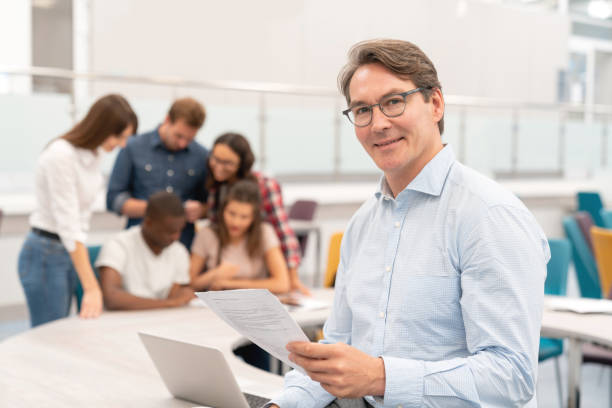 istock Happy male teacher in a classroom holding documents and smiling 1097904300