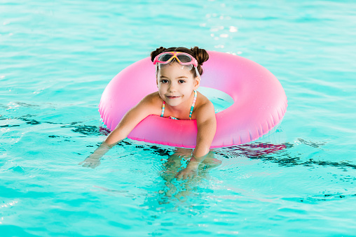 smiling child learning swimming with inflatable ring in swimming pool