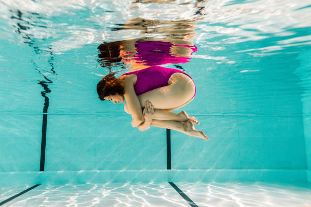 istock woman holding legs while diving underwater in swimming pool 1097906214