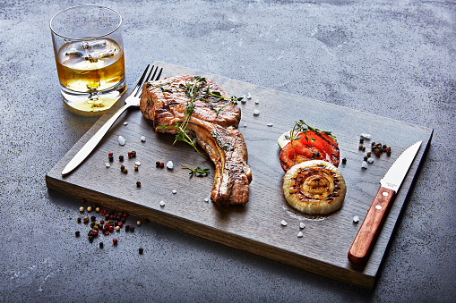 meat on a wooden board with a glass whisky