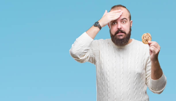istock Young hipster man eating chocolate chips cookie over isolated background stressed with hand on head, shocked with shame and surprise face, angry and frustrated. Fear and upset for mistake. 1097917562