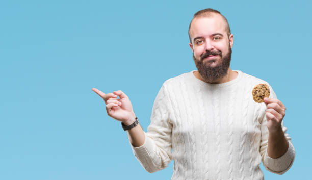 istock Young hipster man eating chocolate chips cookie over isolated background very happy pointing with hand and finger to the side 1097917928