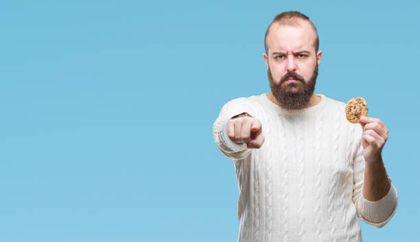 istock Young hipster man eating chocolate chips cookie over isolated background pointing with finger to the camera and to you, hand sign, positive and confident gesture from the front 1097918010