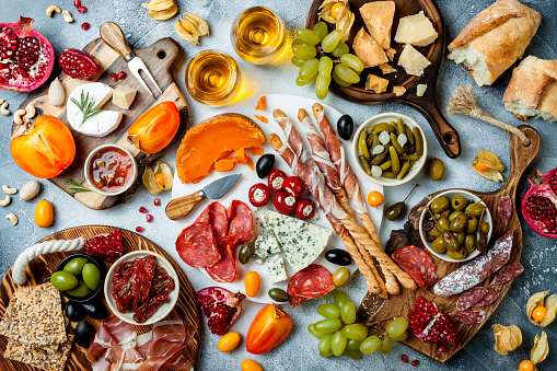 Appetizers table with antipasti snacks and wine in glasses. Authentic traditional spanish tapas set, cheese and meat platter over grey concrete background. Top view