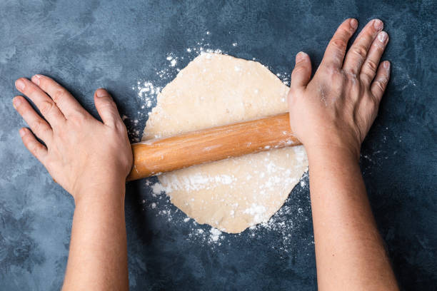 istock Female hands rolling dough on a table with a wooden rolling pin. Top view. Flat lay. 1097950510