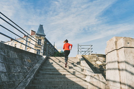 young sportswoman in red sports dress running up stairs outdoors in city