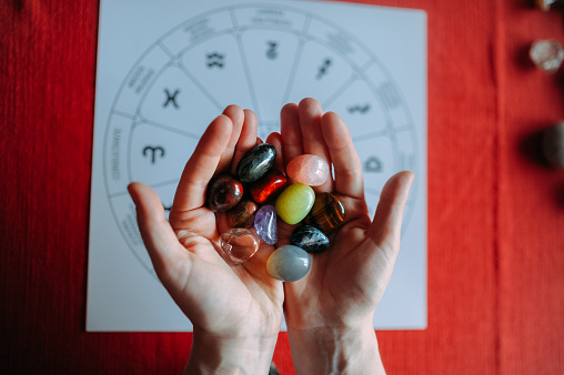 young woman hands showing group of colorful crystal stones during tarot reading with red background