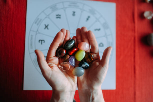 mãos de mulher mostrando o grupo de pedras de cristal colorido durante tarô lendo com fundo vermelho - chakra crystal recovery spirituality - fotografias e filmes do acervo