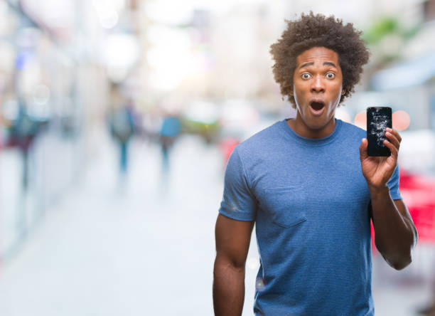 Afro american man holding broken smartphone over isolated background scared in shock with a surprise face, afraid and excited with fear expression