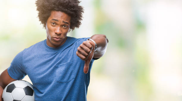 афро-американский человек, держащий футбольный мяч над изолированным фоном с сердитым лицом, отрицательный знак, показывающий неприязнь с  - football human hand holding american football стоковые фото и изображения