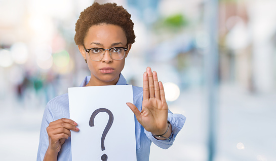 Young african american woman holding paper with question mark over isolated background with open hand doing stop sign with serious and confident expression, defense gesture