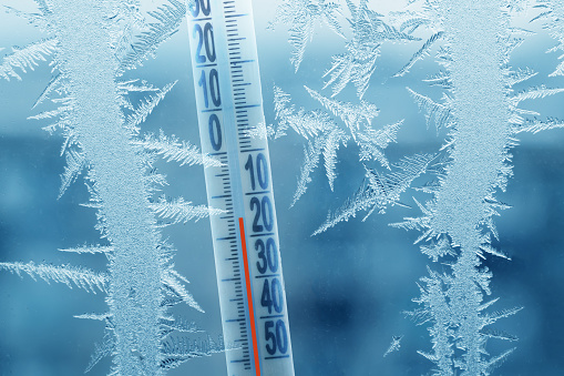 Frosty winter window with ice patterns and a thermometer showing a minus temperature.