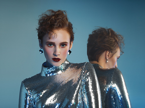 Woman in futuristic sequin jumpsuit and her mirror reflection