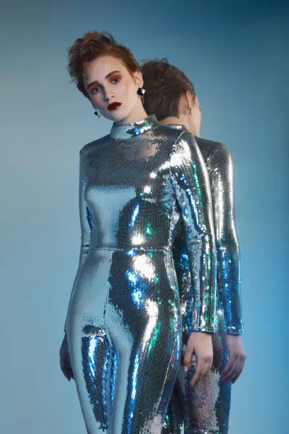 Woman in futuristic sequin jumpsuit and her mirror reflection